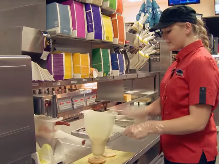 Each cheeseburger receives a measured shot of mustard and ketchup from a dispenser.