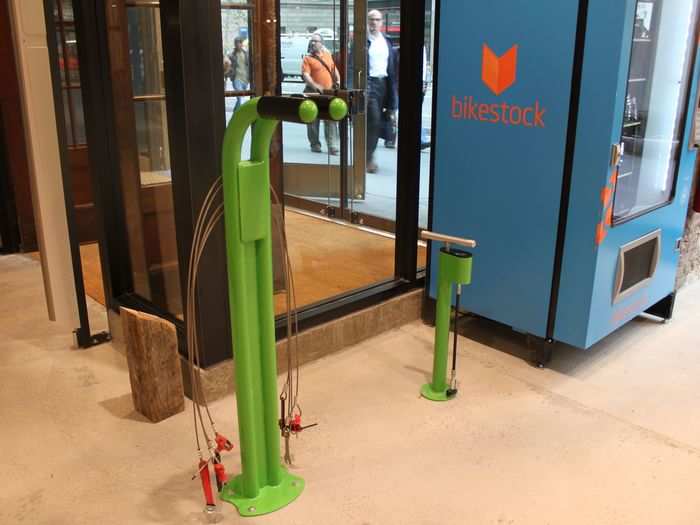 Before leaving the store, customers can make quick bike repairs. The vending machine pictured sells bike parts and one of the green posts is an air pump, while the other features a half dozen bike tools.