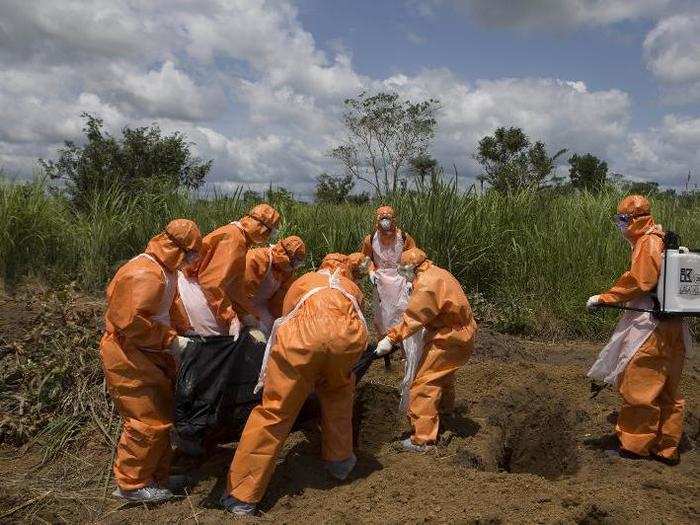 The workers remain in head-to-toe protective gear as they prepare to inter the bodies of victims.