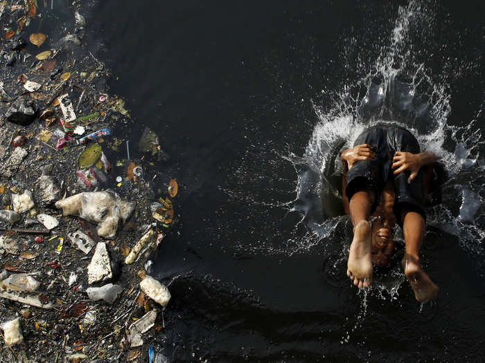 This boy cannonballs into a polluted river in Jakarta, Indonesia, while piles of garbage drift by next to him.