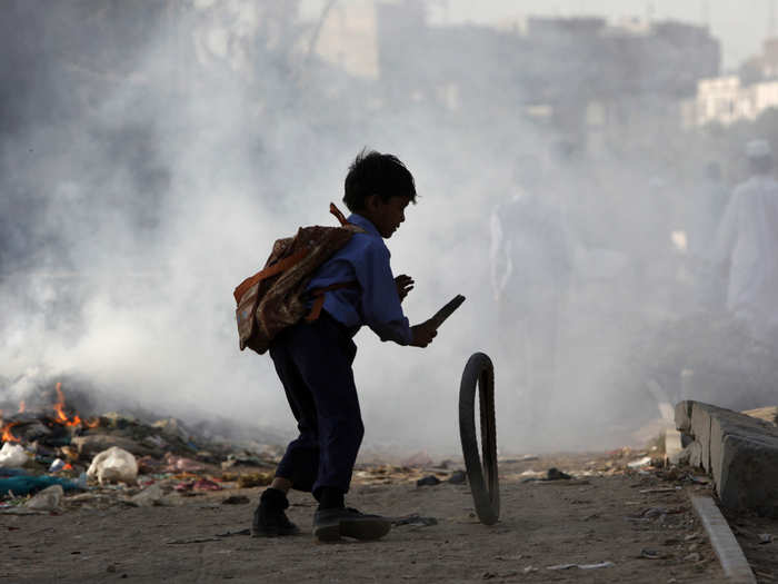 Despite it all, children are surprisingly adept at finding ways to entertain themselves amidst all the rubbish. This little boy, also in a slum area of Karachi, Pakistan, makes his own toys from the garbage that surrounds him. Here, he plays with a tire while other slum residents burn garbage in the background.