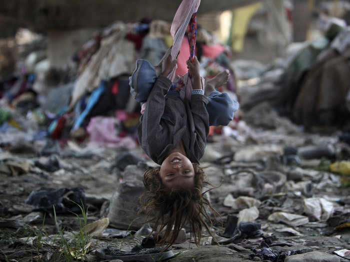 A child swings under a bridge amidst stacks of garbage in Kathmandu, Nepal.