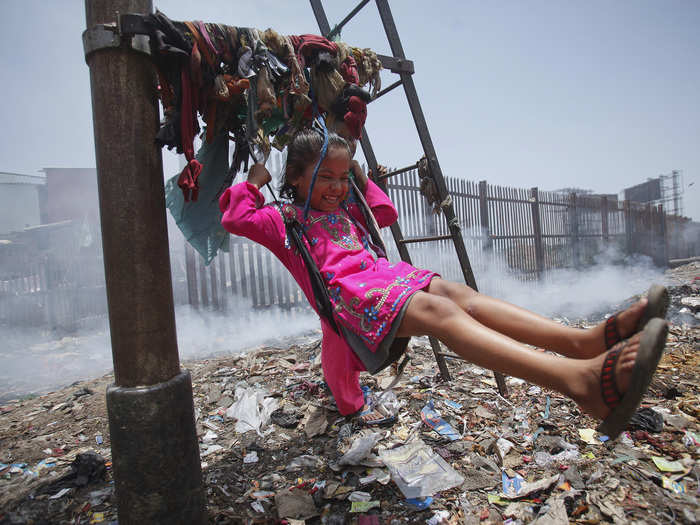 This girl happily swings while smoke rises from the garbage dump behind her in Mumbai, India.