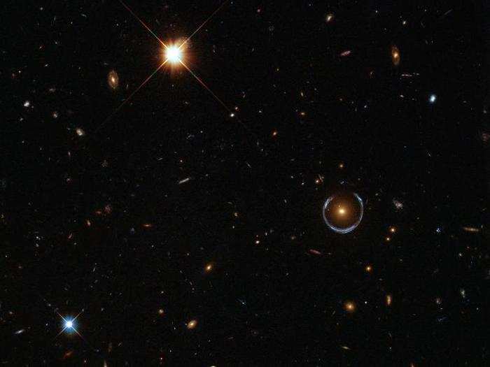 Believe it or not, this is a real Hubble image, and that bizarre blue ring toward the right is an optical illusion produced when gravity bends light in a phenomenon called gravitational lensing. Astronomers have used this technique, called gravitational lensing, to discover some of the smallest, faintest, most distant galaxies in our universe.