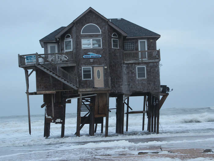 Even the base line scenario for rising sea levels would flood beachfront roads and homes and devastate the tourism and real estate industries. Here, a beachfront home on the eroded shoreline tilts on its supports.