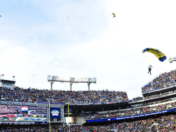 A formation of U.S. Army helicopters flies over M&T Bank Stadium, and service members from the Navy Leapfrogs and the Army Golden Knights parachute teams make a grand entrance.