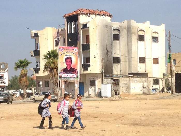 Here, schoolgirls walk past another billboard and remnants of the conflict outside of Rafah.