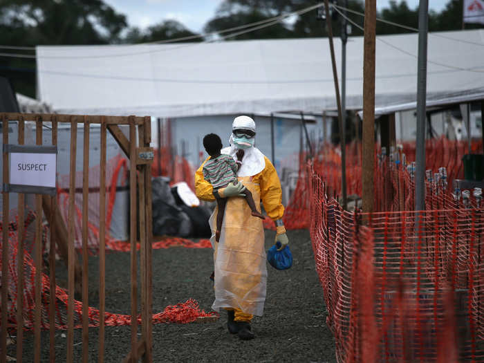 A Doctors Without Borders health worker in protective clothing carries a child suspected of having Ebola in the group