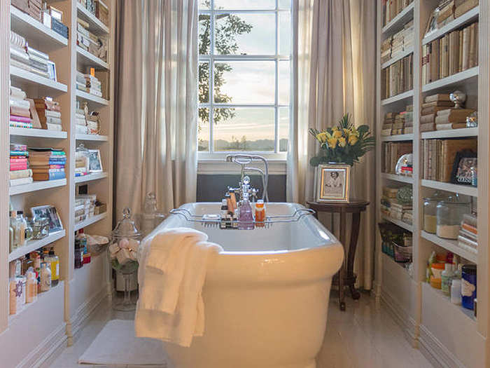 The bathtub is surrounded by books and has a lovely view outside.