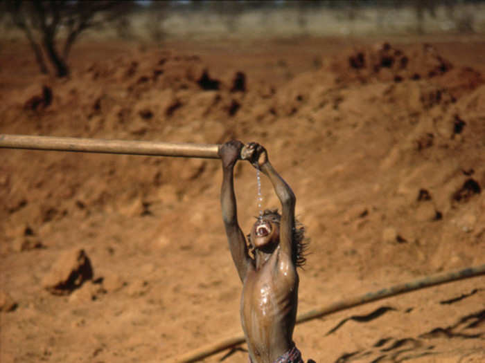 On some days, it was 110 degrees Fahrenheit in the shade. Here, a boy catches some relief from the end of a dripping pipe.