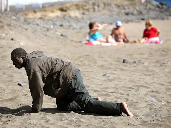 A would-be immigrant crawls on the beach after his arrival on a makeshift boat on the Gran Tarajal beach in Spain