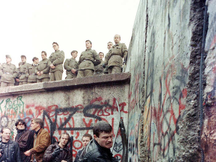 A demonstrator pounds away at the Berlin Wall as East Berlin border guards look on from above the Brandenburg Gate in Berlin in November, 1989.