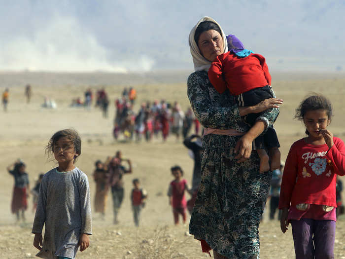 Displaced people from the minority Yazidi sect, fleeing violence from forces loyal to the Islamic State in Sinjar town, walk towards the Syrian border on the outskirts of Sinjar mountain near the Syrian border town of Elierbeh of Al-Hasakah Governorate in 2014. The Islamic State, which had declared a caliphate in parts of Iraq and Syria, prompted tens of thousands of Yazidis and Christians to flee for their lives during their push to within a 30-minute drive of the Kurdish regional capital Arbil.