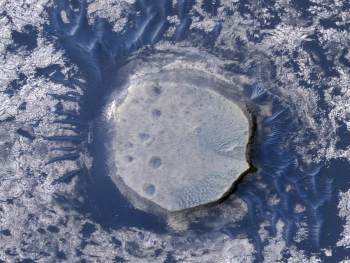 This is what is referred to as an inverted crater. The dark-blue dunes circling the crater come from the basaltic volcanic rock. The inverted crater is in the Arabia Terra region and measures 800 feet across — about the length of 5 Olympic-sized swimming pools.