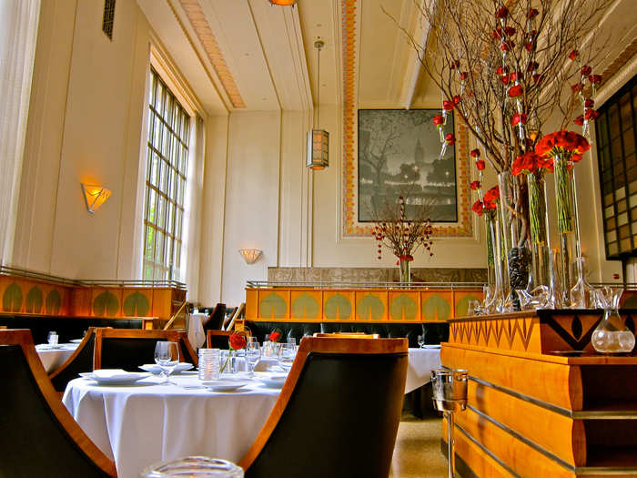 The Art Deco-styled dining room features floor-to-ceiling windows and whimsical floral arrangements that reach to the high ceilings.