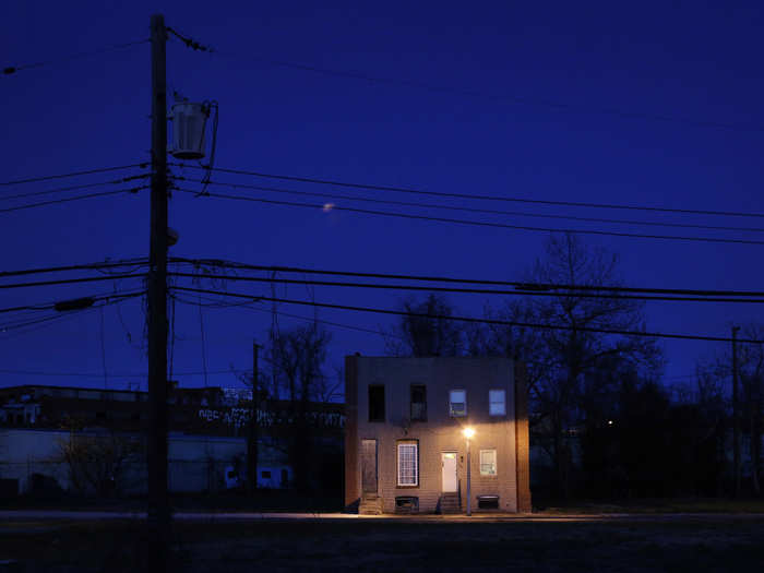 Many properties have been left to the elements. Here, two row houses, one boarded up, the other occupied, are surrounded by vacant lots at dusk in Baltimore.