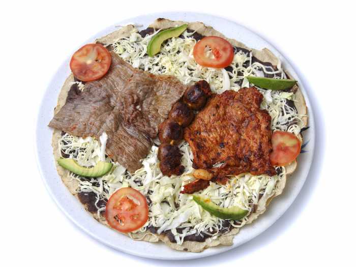 Considered an iconic dish of the state of Oaxaca, Tlayuda is a large, thin, partially-fried tortilla covered in refried beans, asiento (unrefined pork lard), lettuce, avocado, shredded meat, Oaxaca cheese and salsa.