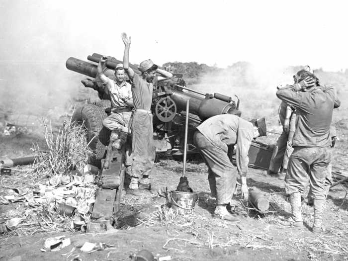 Wearing hardly any protective gear, Marine artillerymen plug their ears after launching a 155mm Howitzer in northern Iwo Jima.