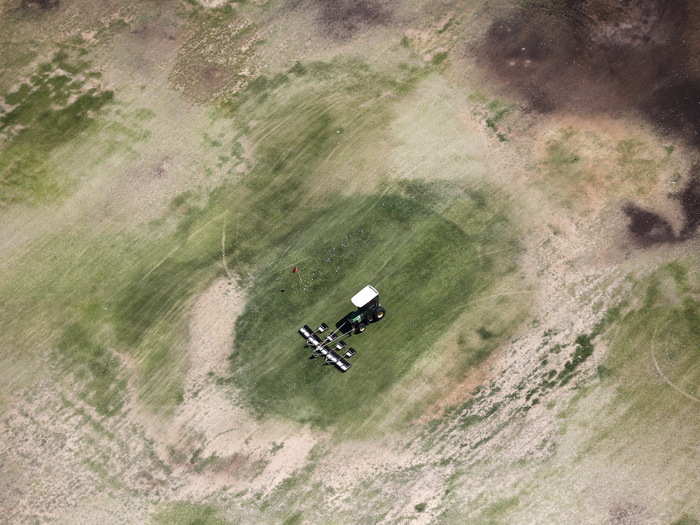 A tractor collects golf balls on a parched driving range in Palm Springs. According to new state regulations introduced May 5, communities like Palm Springs — where residents use more than 165 gallons of water per person per day — would have to cut back their usage by 35%.