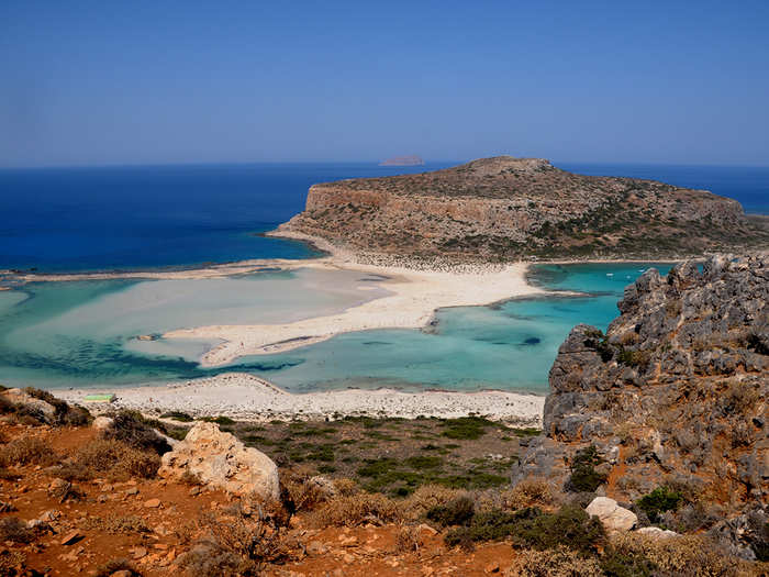 The remote lagoon of Balos, Greece, boasts white sand beaches, electric blue waters, and rare species of flora and fauna. Accessible by a ferry or a three-hour hike over dry terrain, it