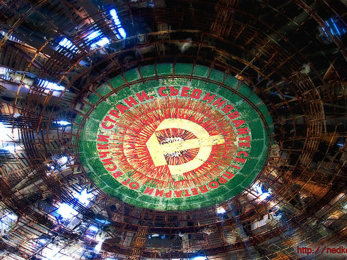 The ceiling features a massive hammer and sickle painted on a round metal plate. The words around the symbol read, "Workers of the world, unite!"