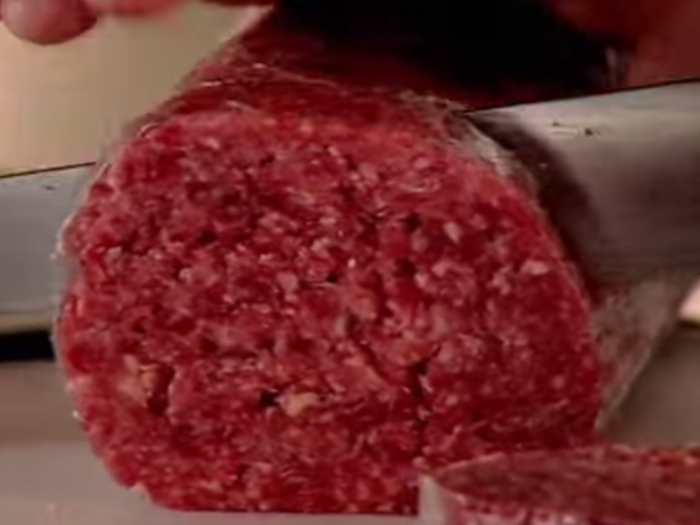 The chef slices his meat roll into perfectly round patties.