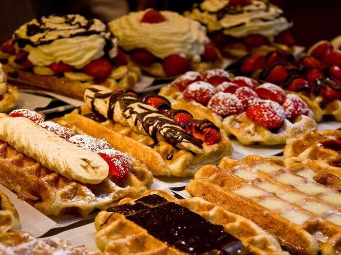 Belgian waffles are made fresh before being baked in a waffle iron and topped with chocolate, fruits, whipped cream, and sugar.