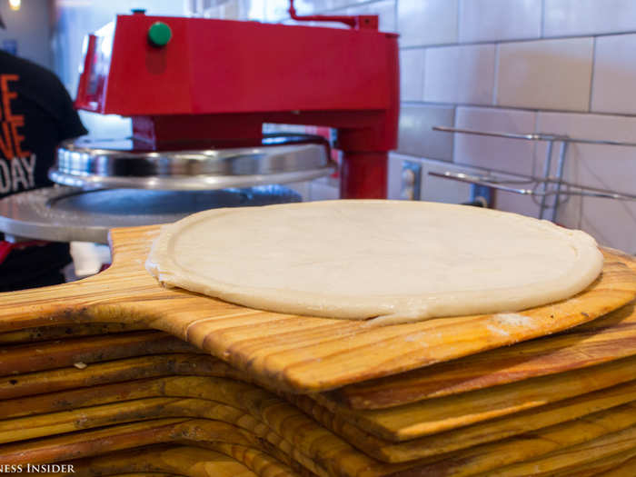 Seconds later, he lifted the dough off the plate and placed it on a wood peel for transportation down the assembly line.