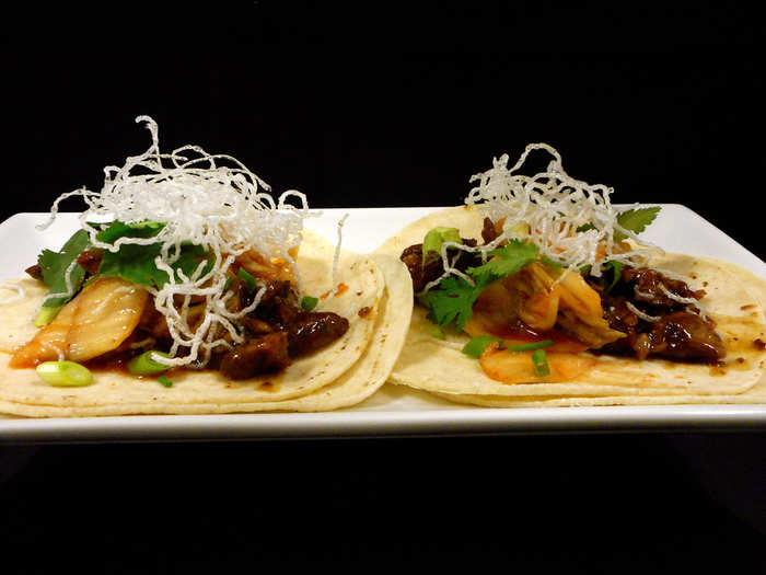 Korean Bar-B-Q Beef Taco: Marinated beef glazed with spicy soy honey, layered with kimchi, topped with crispy rice noodles and served on two flour tortillas.