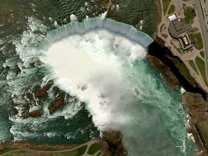 Niagara Falls is the collective name for three waterfalls that straddle the border between Ontario, Canada and the United States. The falls have the highest flow rate of any waterfall in the world, with a vertical drop of more than 165 feet (50 m). The Maid of the Mist boat, visible here, has carried passengers into the rapids immediately below the falls since 1846.