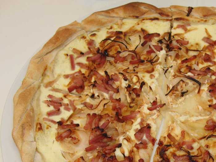 Tarte flambee is a type of crispy, thin-crust pizza that comes from Alsace and is usually topped with crème fraîche, thinly sliced onions, and lardons.