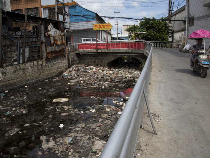 As a result, large amounts of pollutants are released into the air and rivers nearby, contaminating local water supplies. Here, a polluted river flows past a workshop used for processing the plastic components.