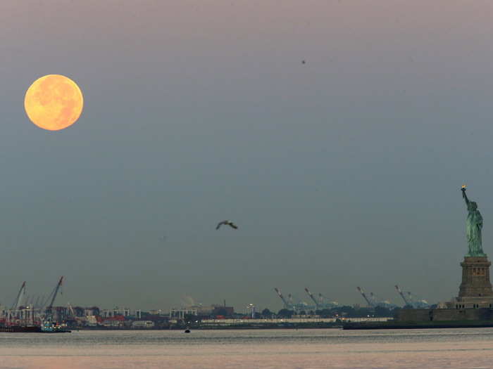 The Moon rises over the Statue of Liberty.