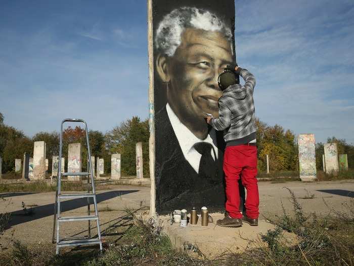 Local artists will often paint portions of the wall. Here, Victor Landeta, a street artists, spray paints a portrait of Nelson Mandela on a segment of the Berlin Wall in Kleinmachnow, Germany.