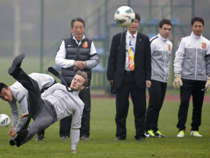 Former England captain David Beckham tumbles as he free kicks at a sports field during his visit in Wuhan, Hubei.