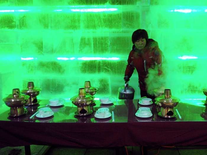 An employee pours boiling water into a pot at a restaurant built with giant ice cubes during an ice festival in Harbin, in China