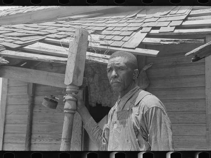 A farmer is pictured on the front porch of his dilapidated home, south of Muskogee, Oklahoma. He