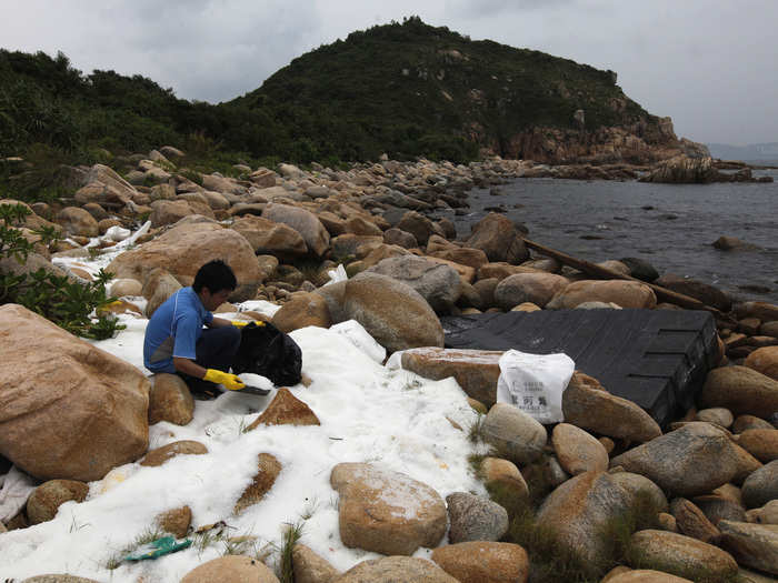 A volunteer clears up plastic pellets on a bank along Hong Kong