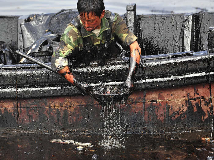 A worker scoops oil near Dalian Port in the Liaoning province of China nine days after a busted pipeline leaked 1,500 metric tons of heavy crude into the water. This photo was taken on July 26, 2010.