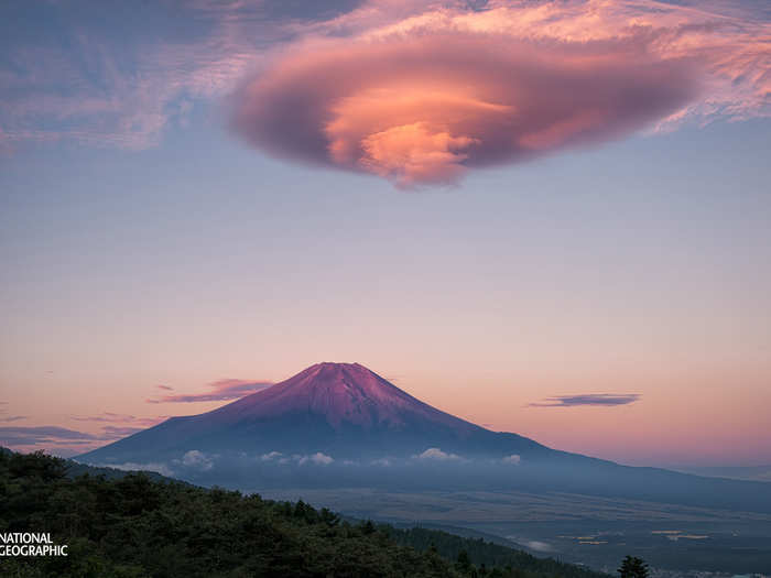 Lenticular clouds glowing pink in the sunrise hover over Mount Fuji in Onuma, Yamanashi, Japan.