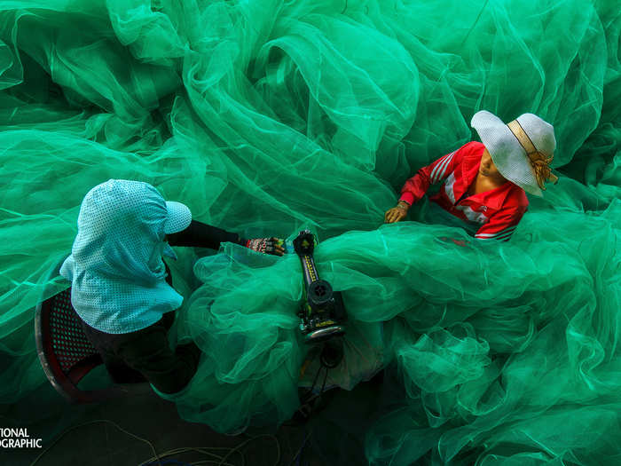 Two women become lost in the fabric of a fishing net in Vinh Hy, Ninh Thuan, Vietnam. They are sewing the net for a new fishing season while their husbands are out fishing.