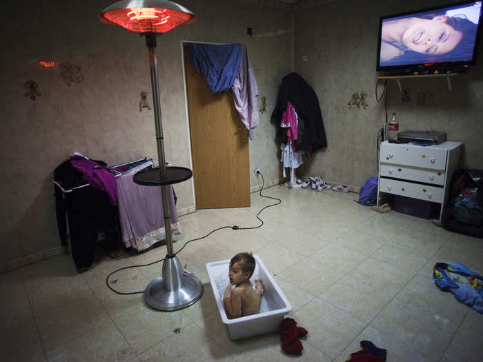 Outside of Madrid, in the gypsy settlement of Puerta de Hierro, a young boy takes a bath while watching TV at his grandparents