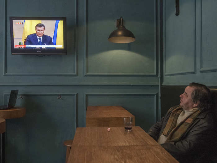 A local resident of Kiev, Ukraine, watches a news broadcast while having a drink.