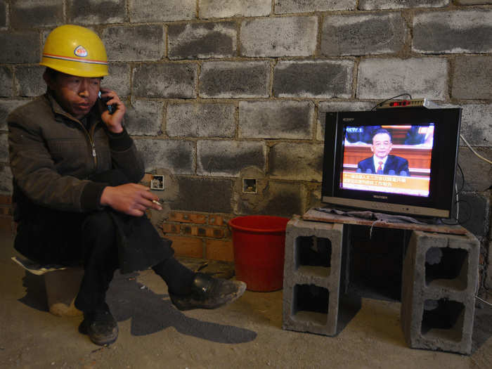 Simultaneously talking on the phone and smoking a cigarette, a labor worker in Changzhi, China catches a government broadcast on TV.