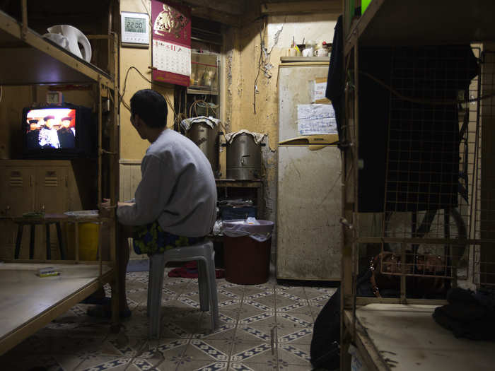 In front of his bed in Hong Kong, a local watches TV in the dim light of a home that he rents for $167 a month.