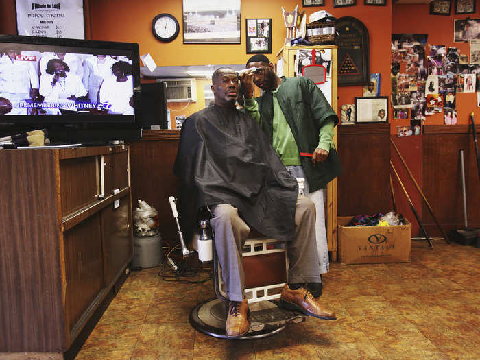 A man gets his haircut in Newark, New Jersey, while the TV plays in the background.