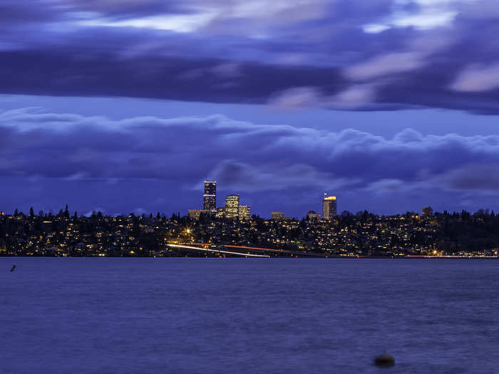 The city of Seattle towers across Lake Washington, illuminated against the night sky.