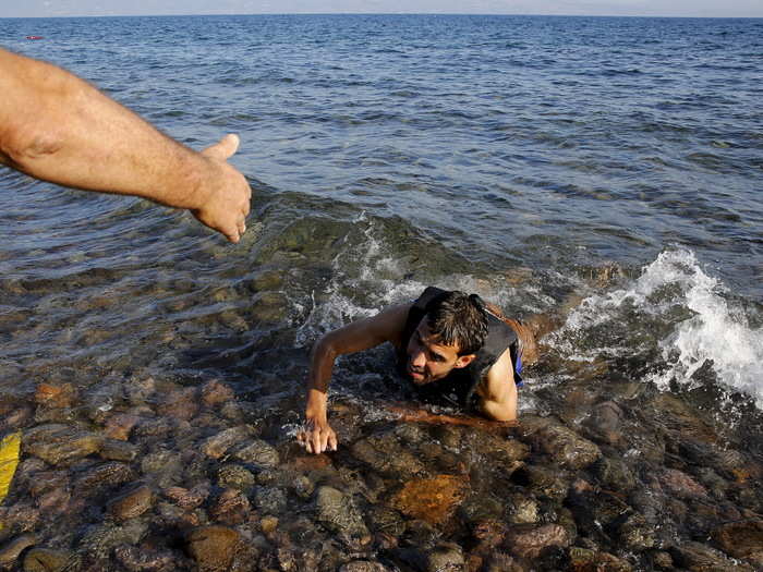 A local man helps a Syrian refugee who jumped off board from a dinghy as he swims exhausted at a beach on the Greek island of Lesbos on September 17, 2015.