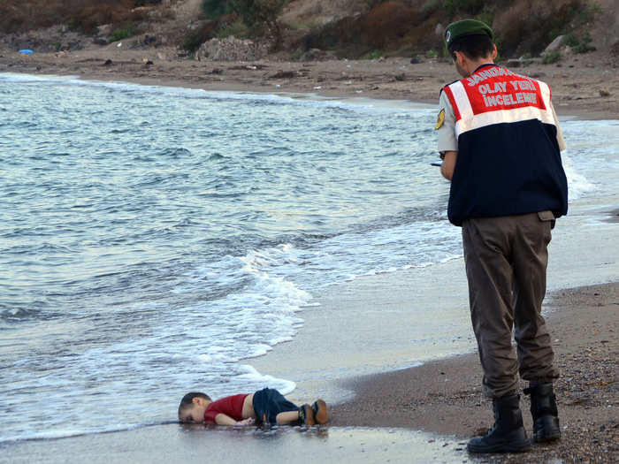 A paramilitary police officer investigates the scene before carrying the lifeless body of Aylan Kurdi, 3, after a number of migrants died and others were reported missing when boats carrying them to the Greek island of Kos capsized near the Turkish resort of Bodrum on September 2, 2015. The tides also washed up the bodies of the boy