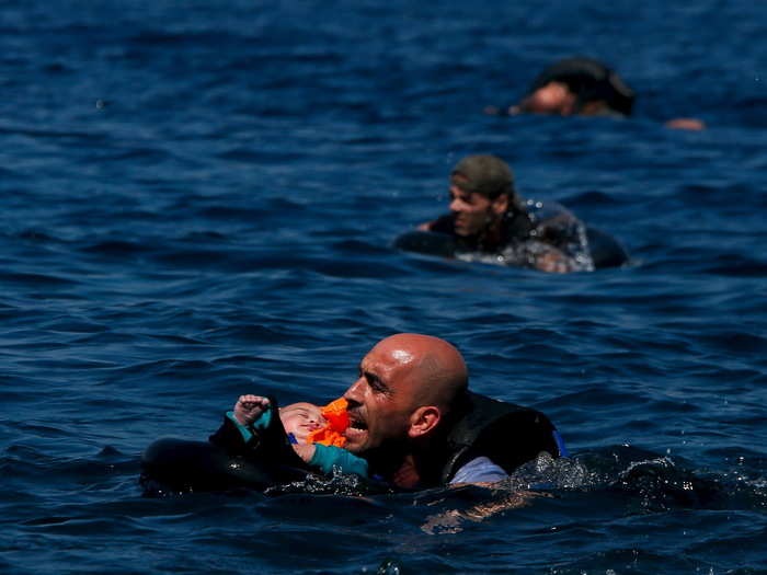 A Syrian refugee holding a baby in a life tube swims towards the shore after their dinghy deflated some 100m away before reaching the Greek island of Lesbos, September 12, 2015.